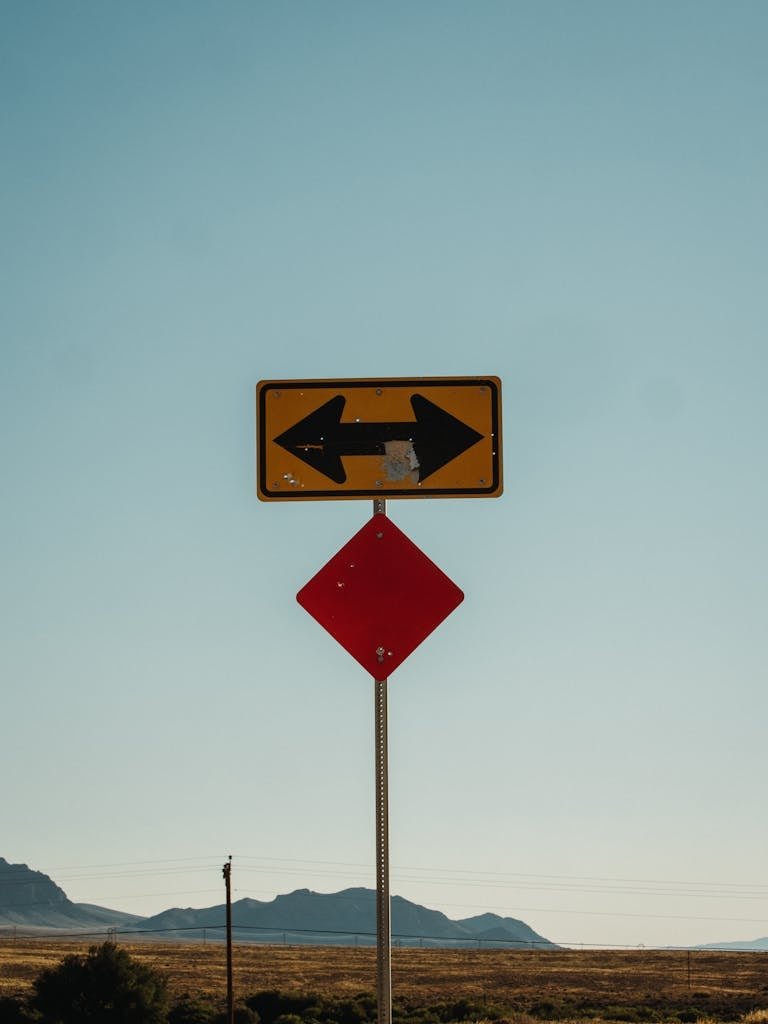 A directional road sign against a clear sky with distant mountains visible.