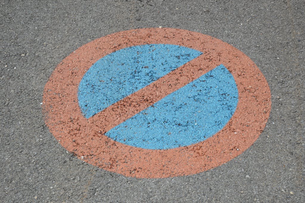 Close-up photo of a no parking sign painted on asphalt with blue and red colors.