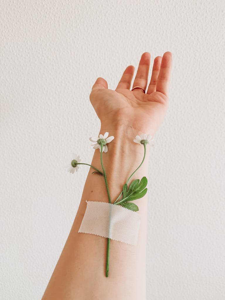 Minimalist image depicting a human arm with a flower taped to it, symbolizing nature and healing.