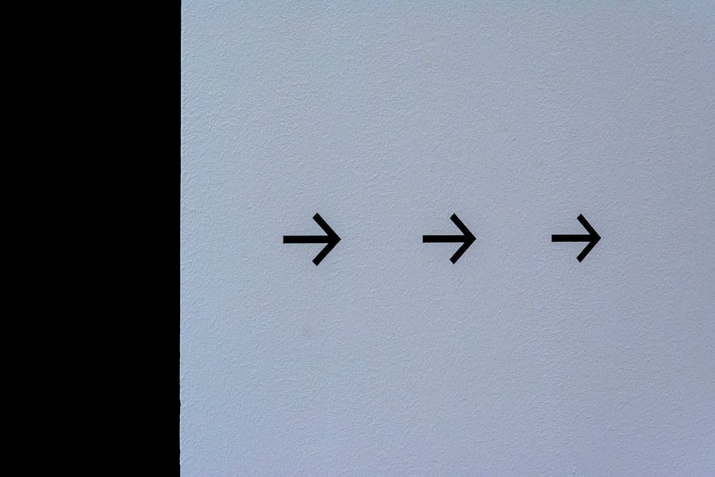 Simple white wall featuring three black arrows pointing right, conveying direction.