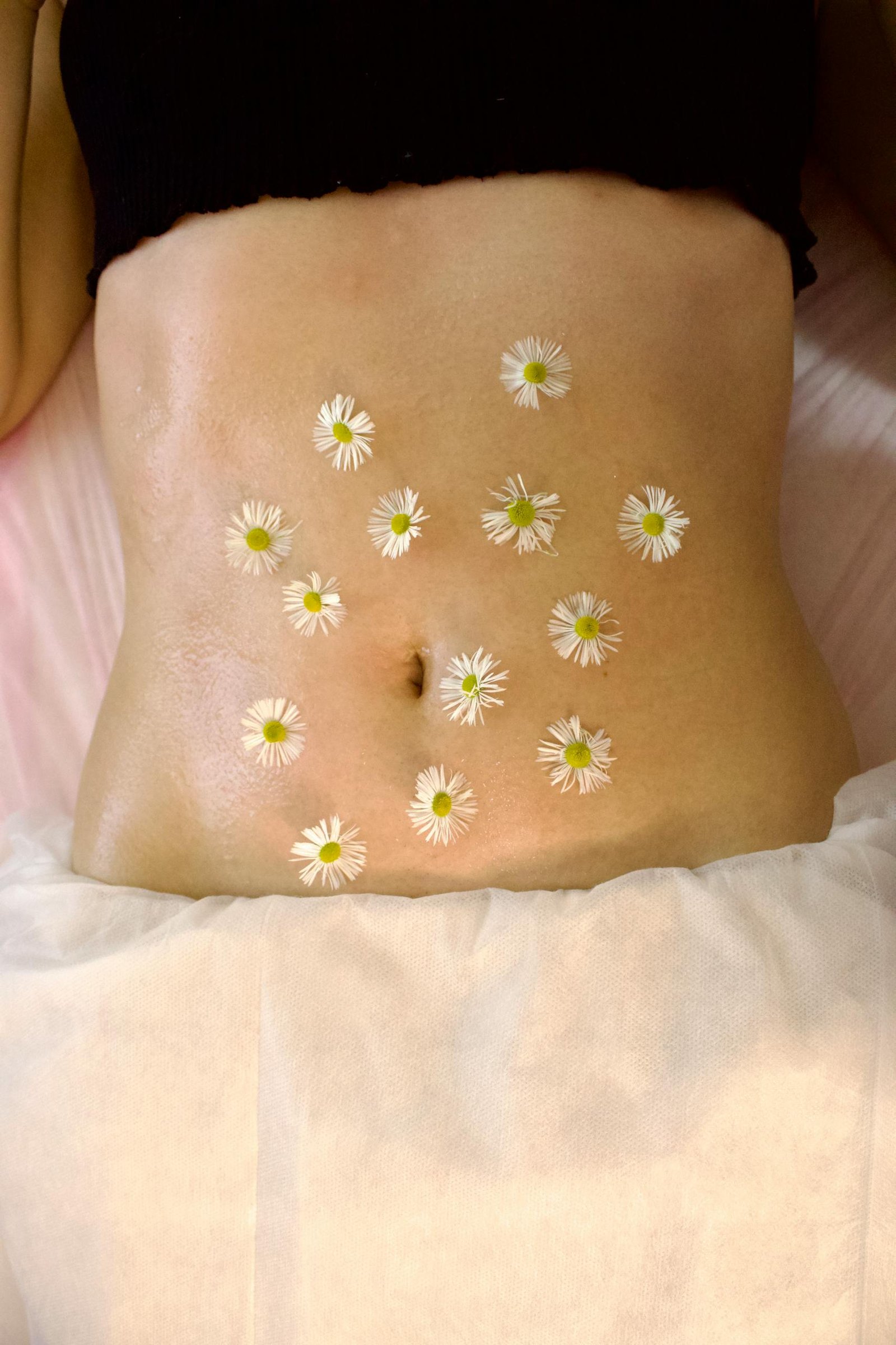 Woman's belly adorned with calming chamomile flowers for relaxation therapy.