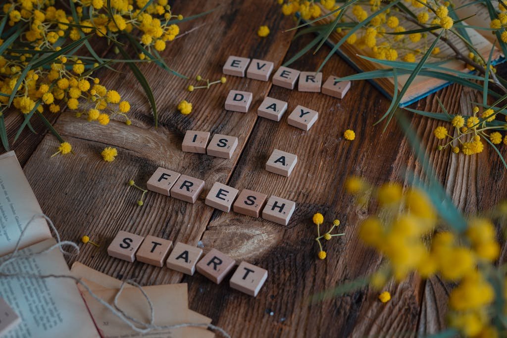 Wooden tiles spell 'Every day is a fresh start' surrounded by yellow flowers on rustic table.
